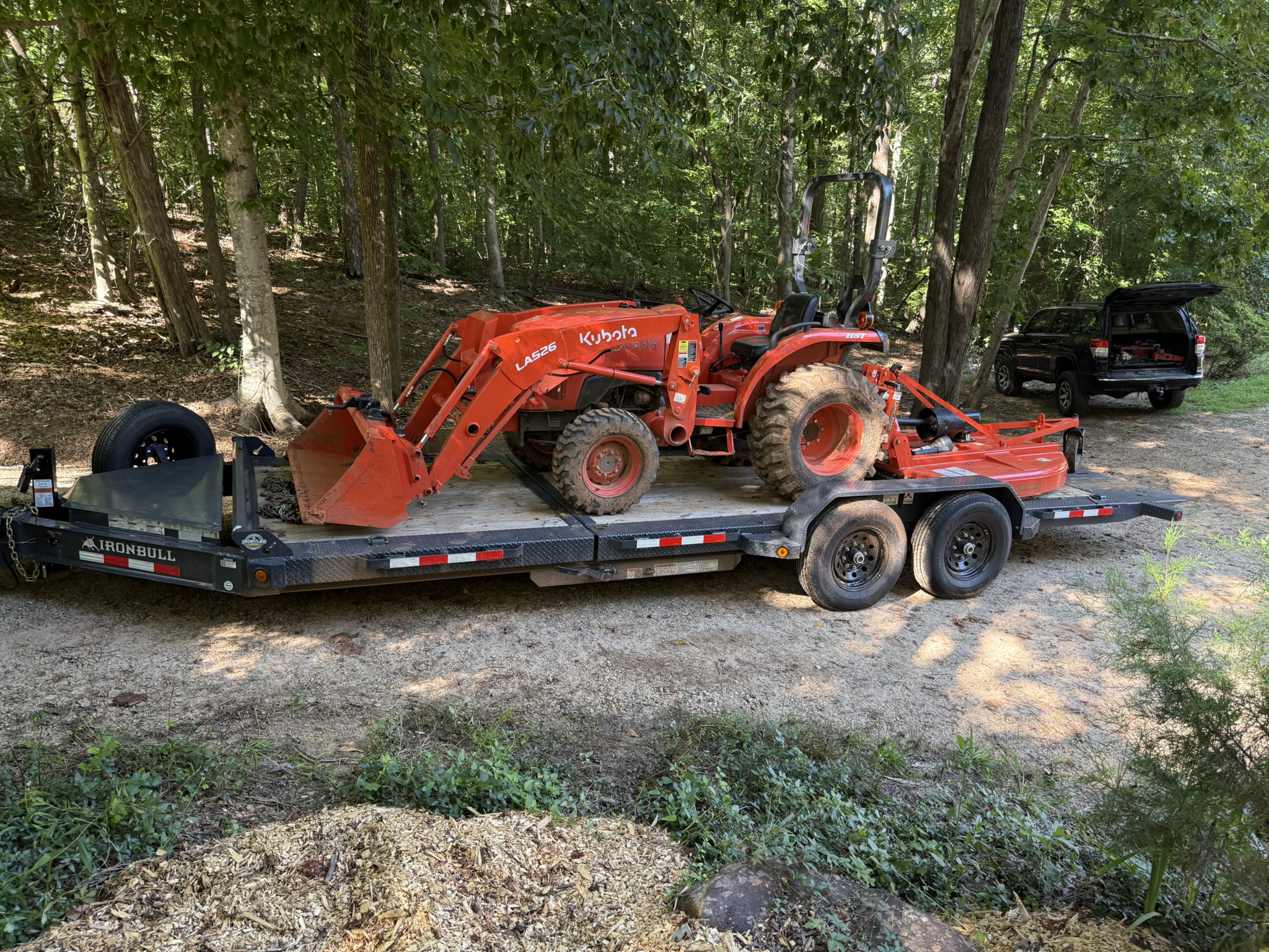 Tilt deck trailer transporting orange Kubota tractor - Construction equipment rental Waxhaw